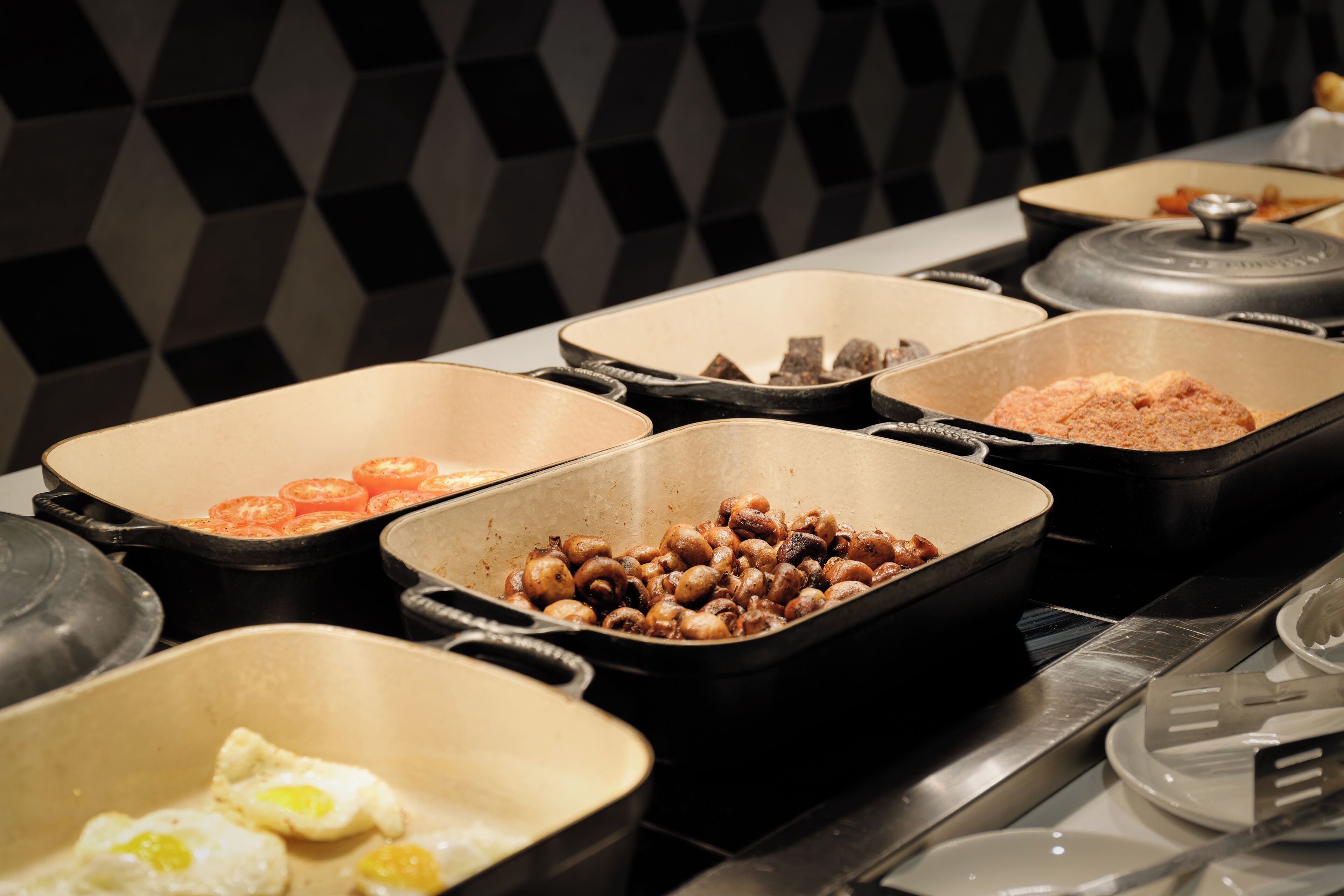 Een buffet met diverse soorten eten, waaronder eieren, champignons en tomaten.