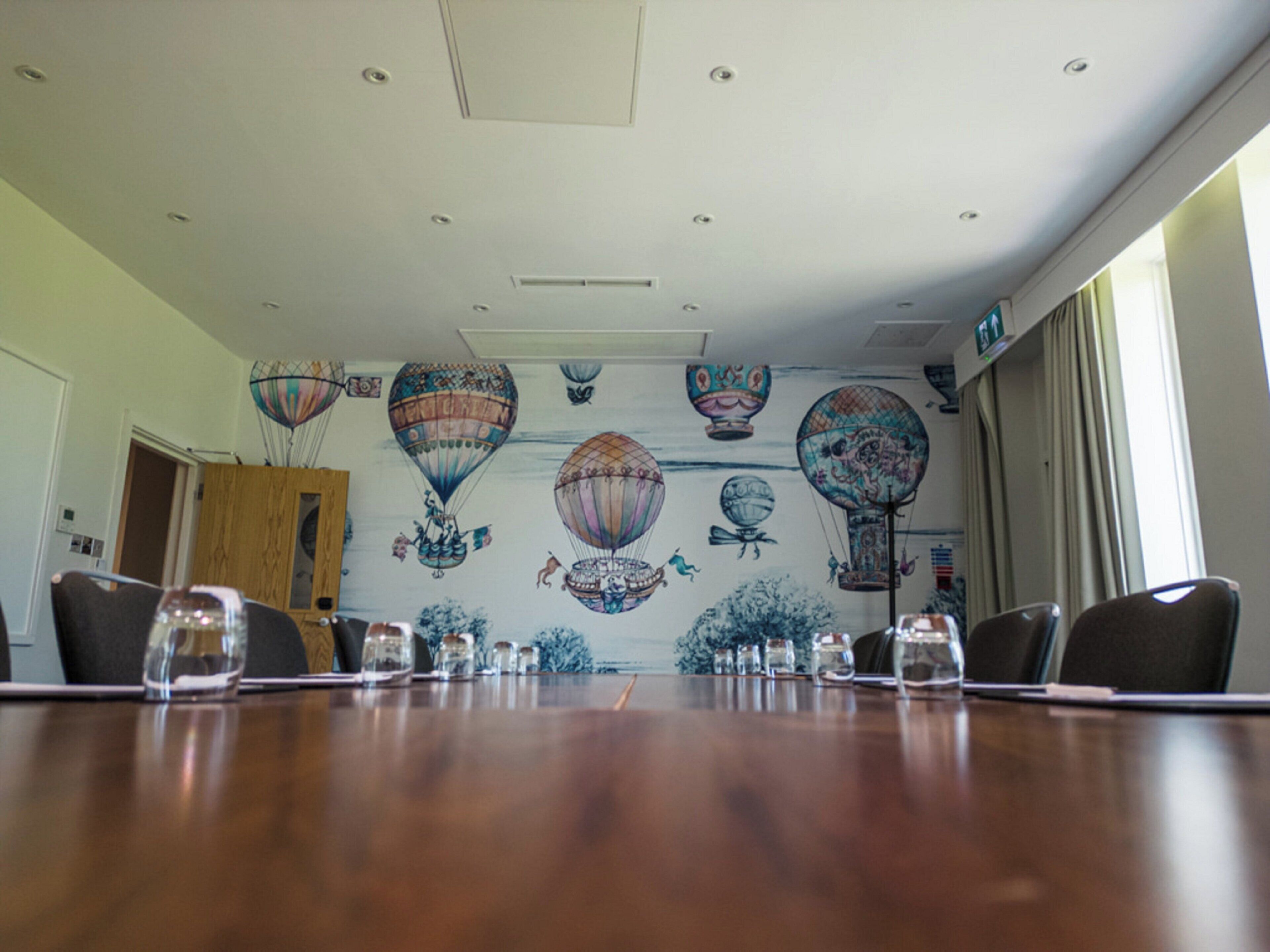 Un salón de conferencias con una larga mesa, sillas y una pared con un mural de globos aerostáticos.