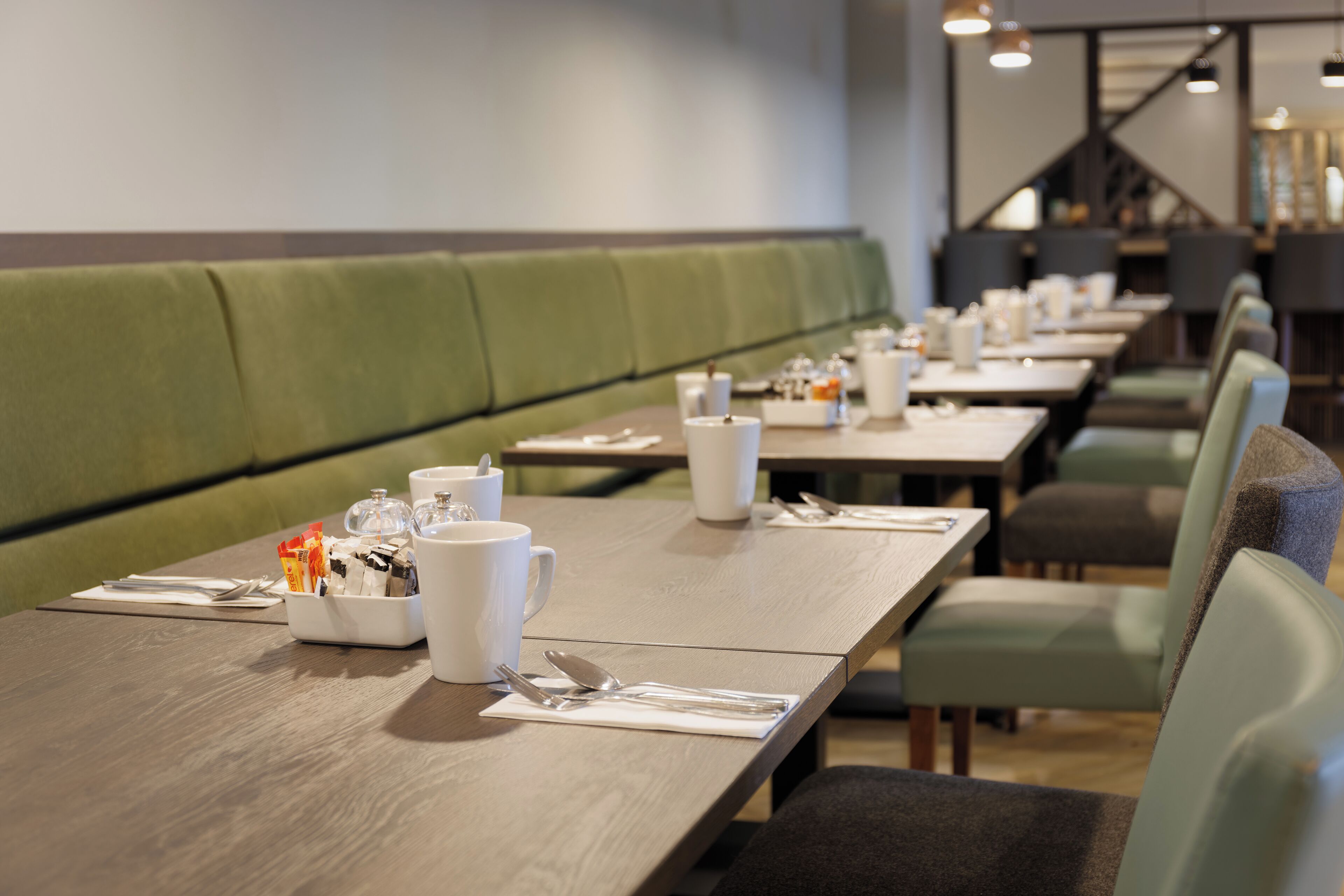 Un restaurante con asientos tapizados en verde y mesas de madera dispuestas con vajilla blanca.