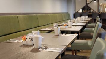 Un restaurante con asientos tapizados en verde y mesas de madera dispuestas con vajilla blanca.