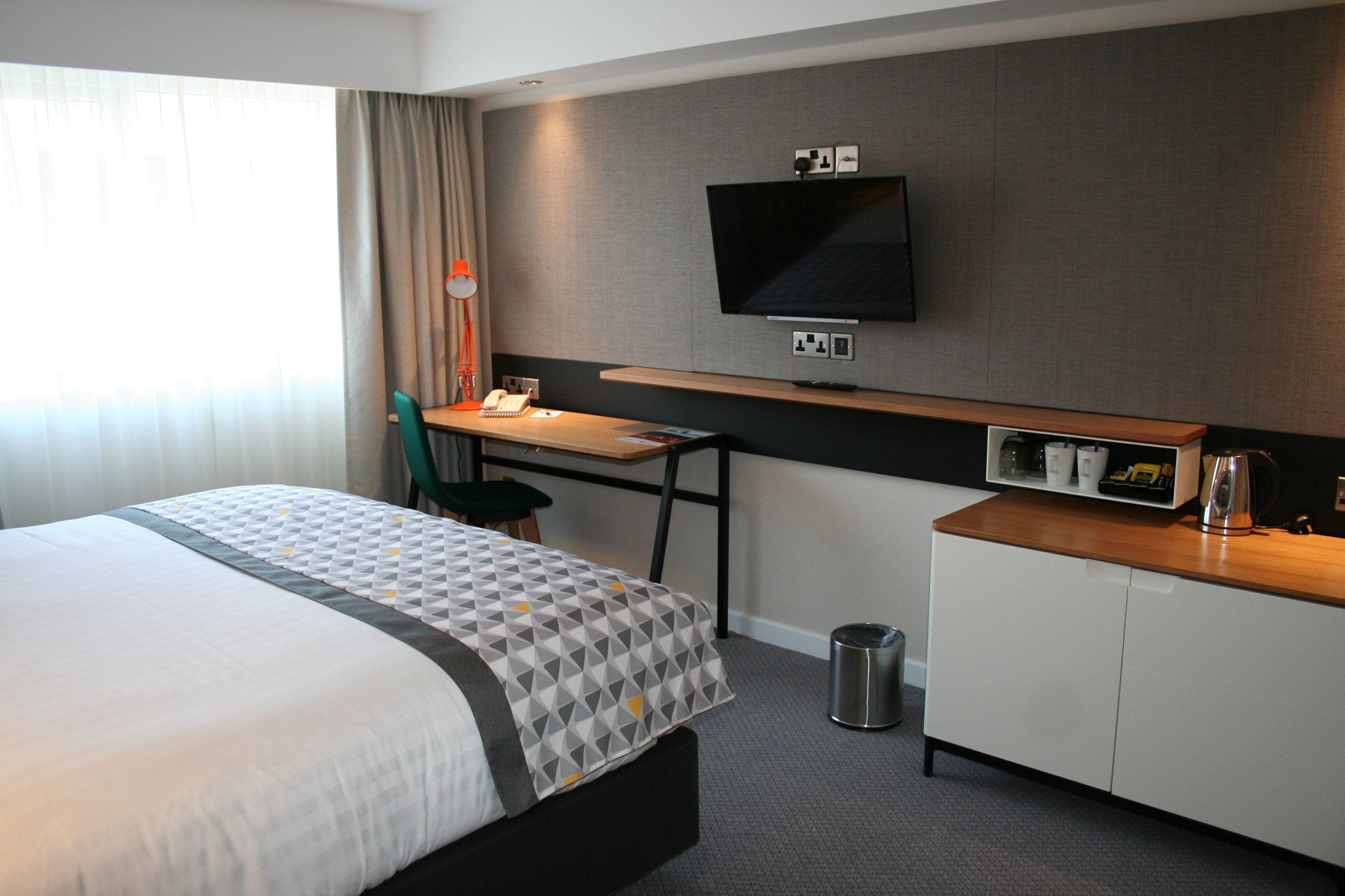A hotel room with a bed, desk, chair, television, and a small kitchenette.