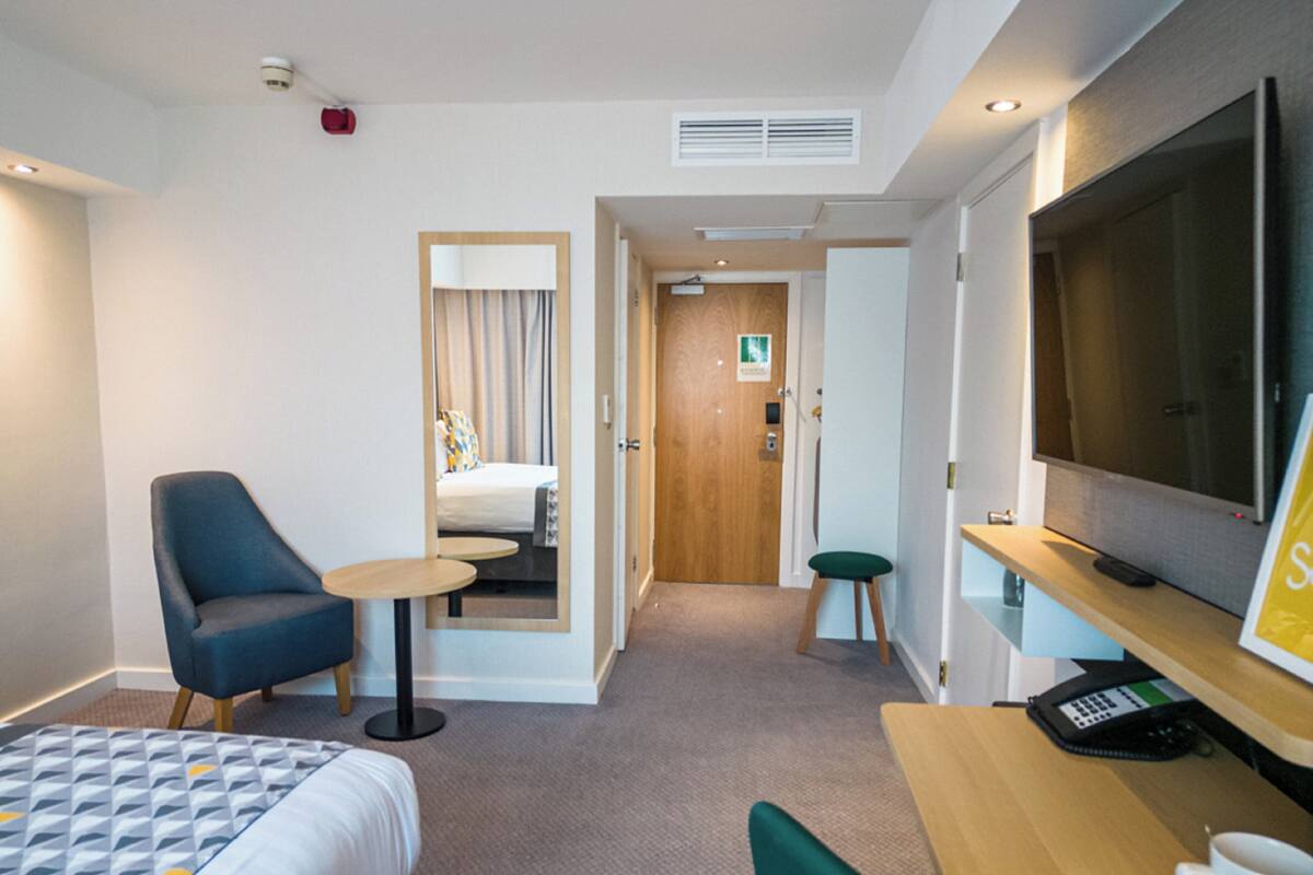 A hotel room with a bed, a desk with a TV, a chair, and a small table.