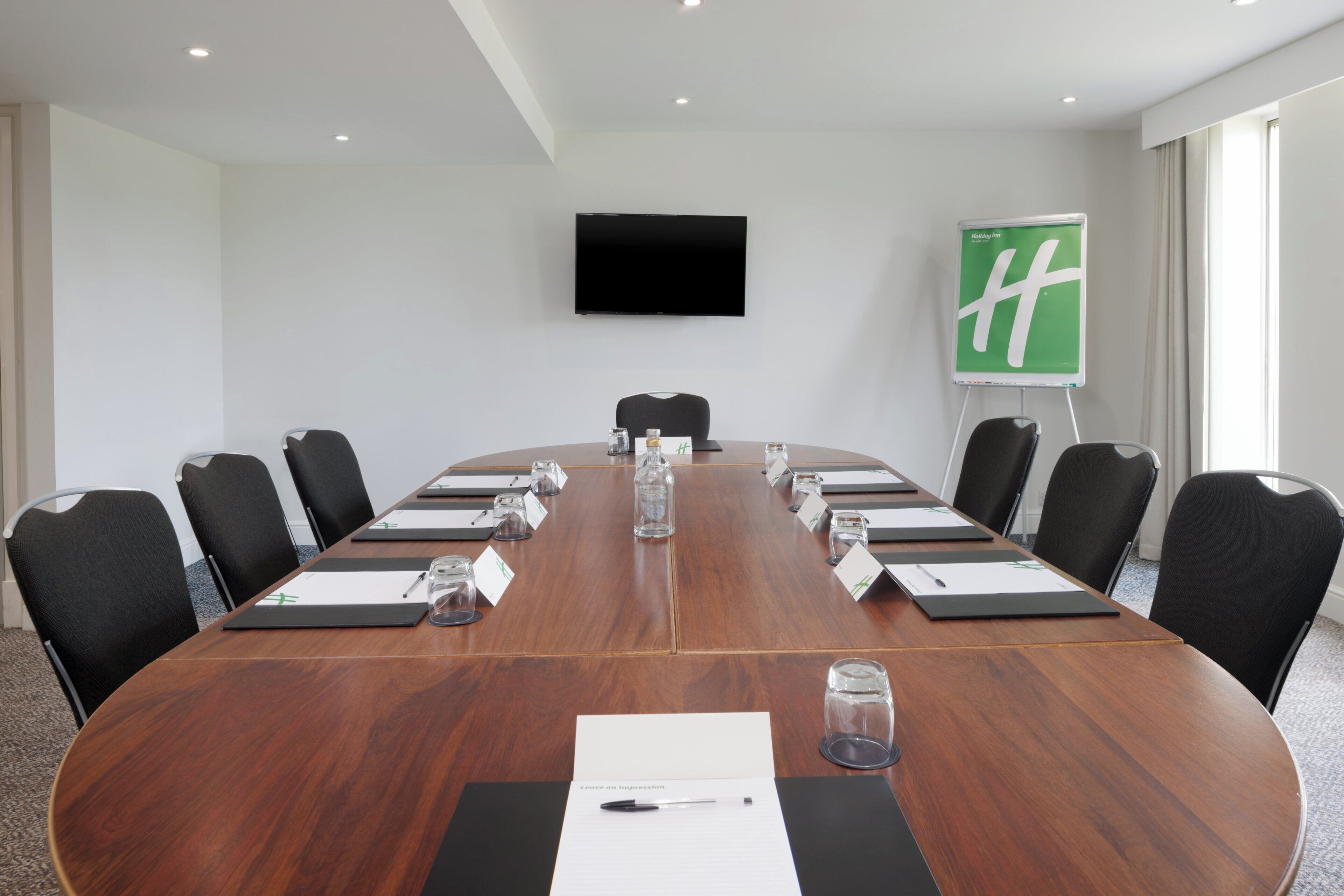 A conference room with a long table, black chairs, nameplates, water glasses, and a whiteboard.