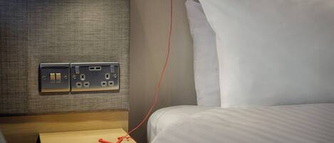 Una habitación de hotel con una cama, una mesita de noche, una lámpara y un enchufe.