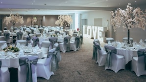 A banquet hall with round tables set for a formal event, adorned with white tablecloths and gray sashes. - Holiday Inn Mansfield - Alfreton by IHG (Alfreton)