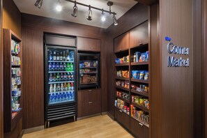 Une petite épicerie de quartier avec un présentoir réfrigéré pour les boissons, des étagères remplies d’en-cas et une enseigne indiquant « The Corner Market ».