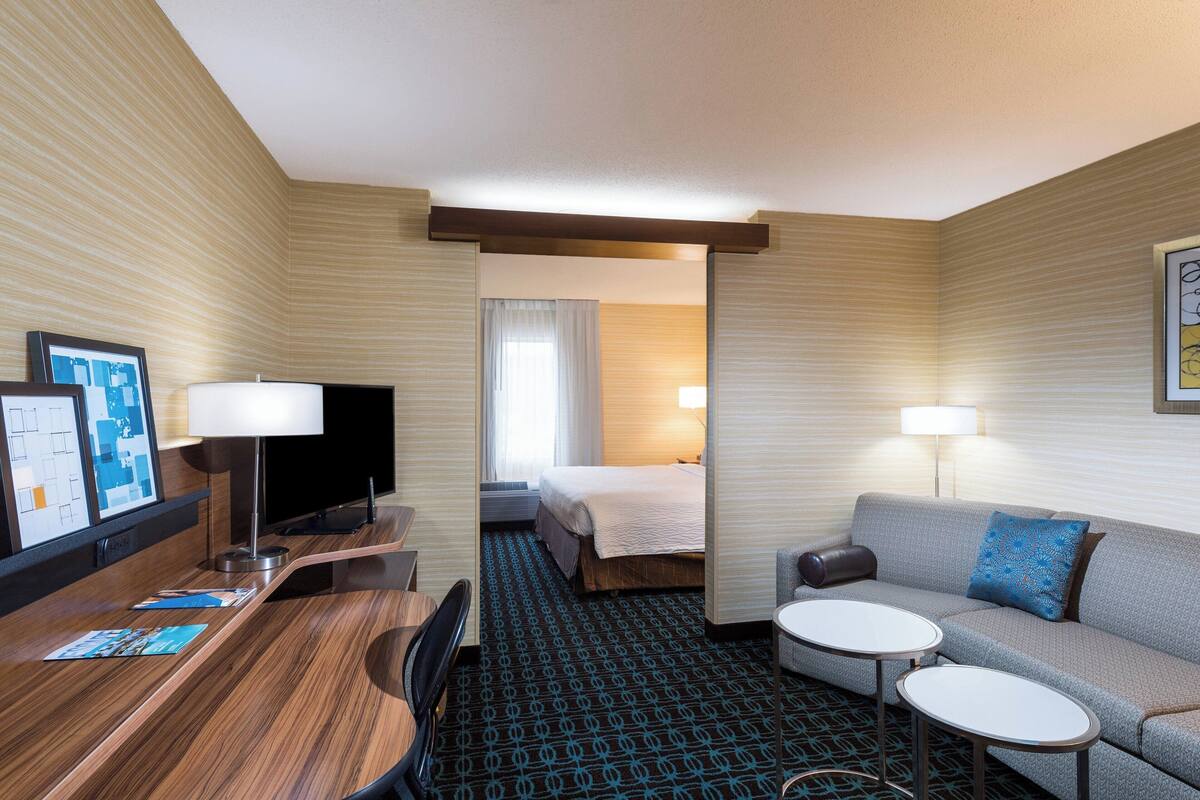 A hotel room with a bed, a sofa, a desk with a chair, a TV, and a small table.