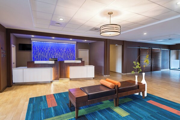 Un área de recepción moderna con un mostrador de madera, una pared decorativa azul grande y una alfombra colorida.