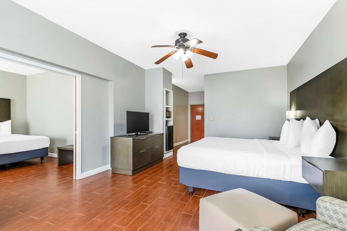 A hotel room with a large bed, a desk, a television, and a ceiling fan.