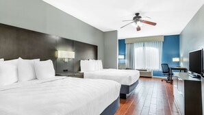 A hotel room with two beds, a desk, a chair, a TV, and a ceiling fan.