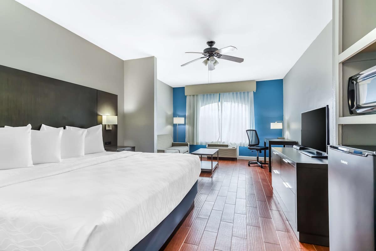 A modern hotel room with a large bed, a desk, a television, and a ceiling fan.