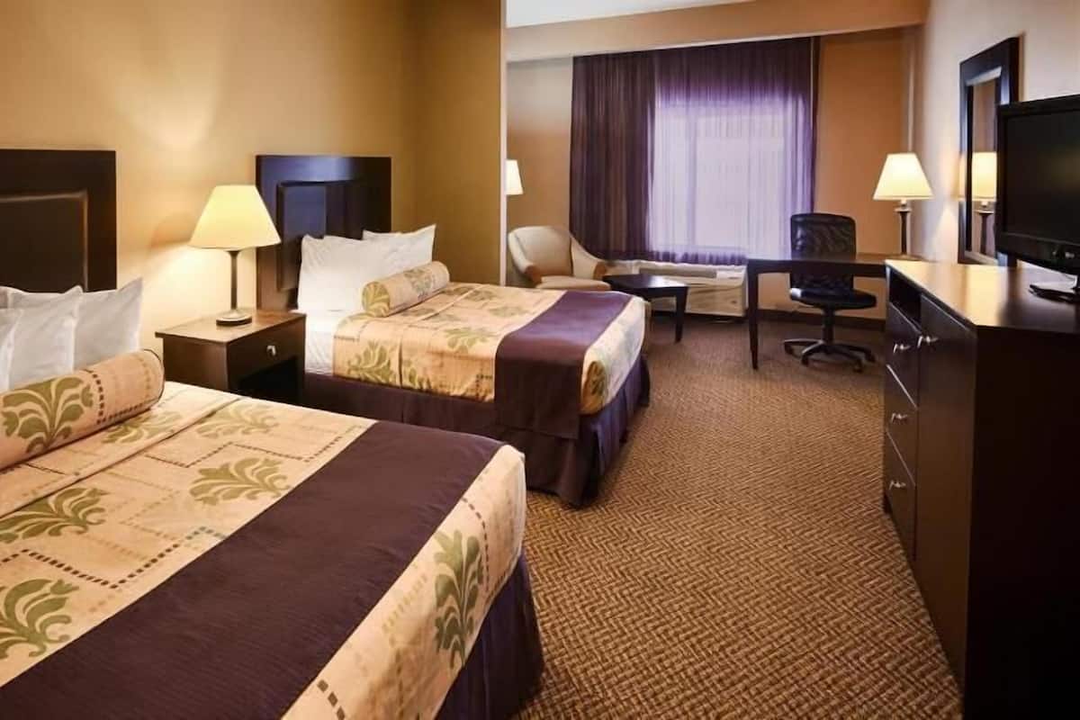 A hotel room with two beds, a desk, a chair, a TV, and a window with curtains.