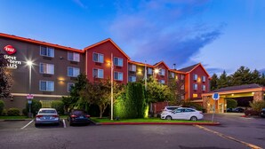 Un hotel de varios pisos con fachada roja y marrón, múltiples ventanas y un estacionamiento con varios automóviles.