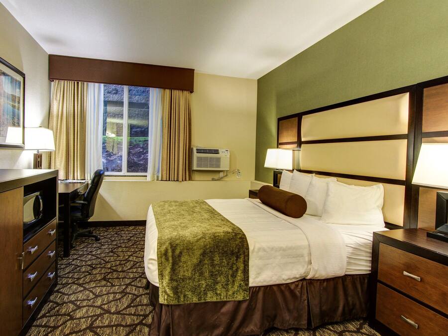 Une chambre d’hôtel équipée d’un lit, d’un bureau, d’une chaise, d’une commode et d’une fenêtre avec des rideaux.