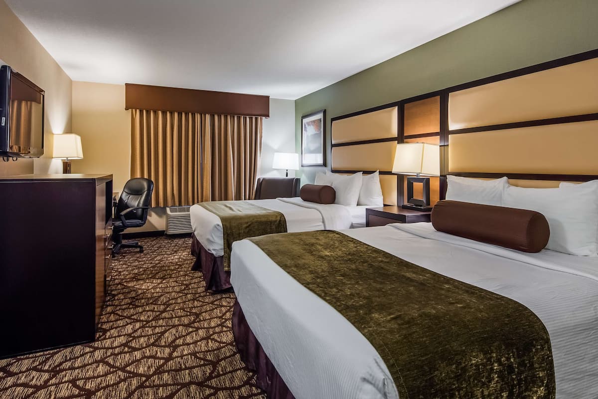 Habitación de hotel con dos camas, un escritorio, una silla, un televisor y una ventana con cortinas.