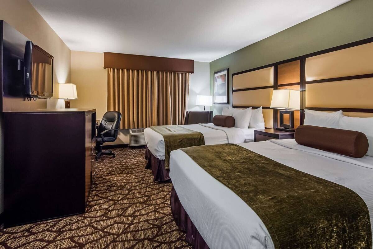 Habitación de hotel con dos camas, un escritorio, una silla, un televisor y una ventana con cortinas.