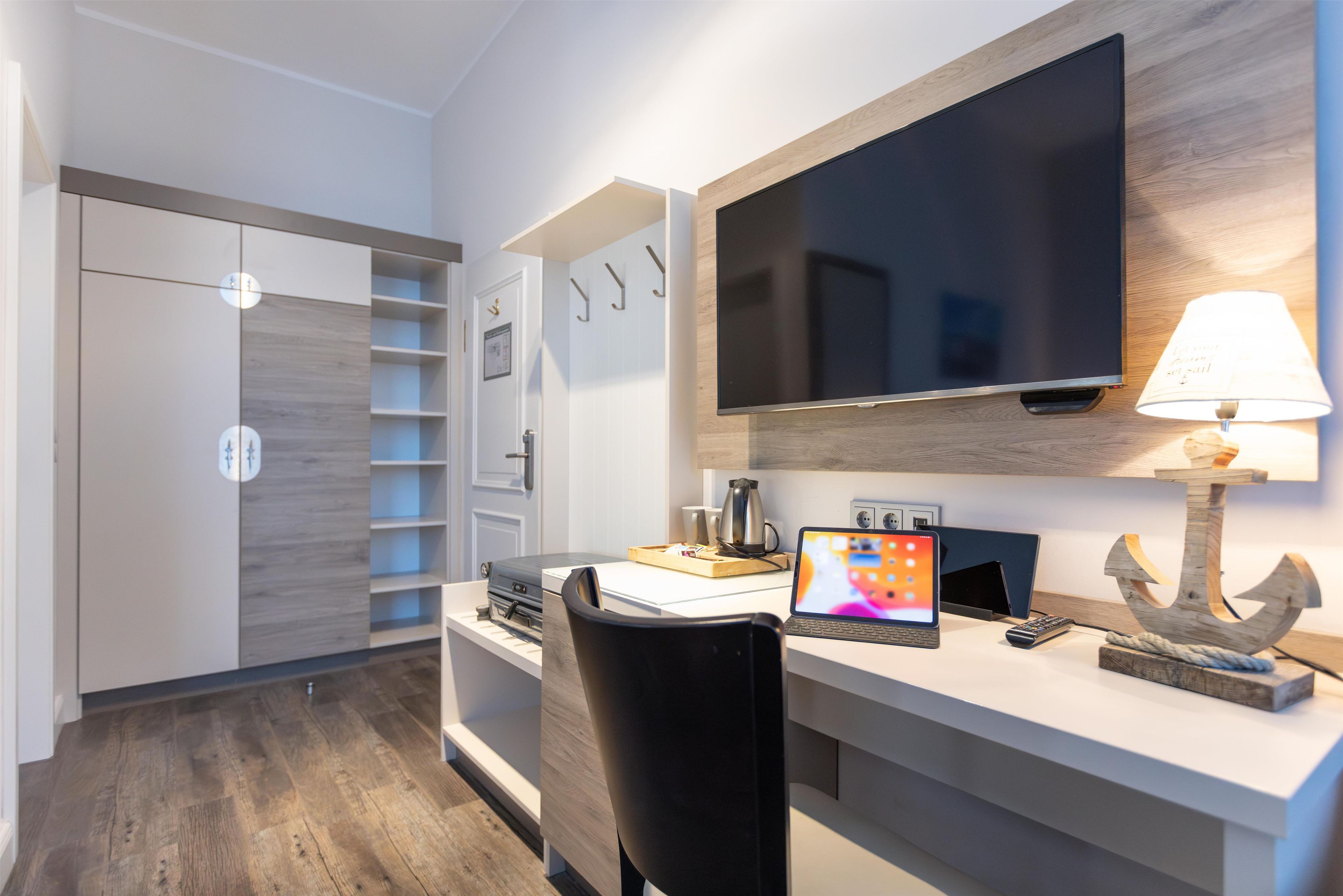 Un dormitorio moderno con una televisión de pantalla plana, un escritorio con una computadora portátil, una cafetera y una silla.
