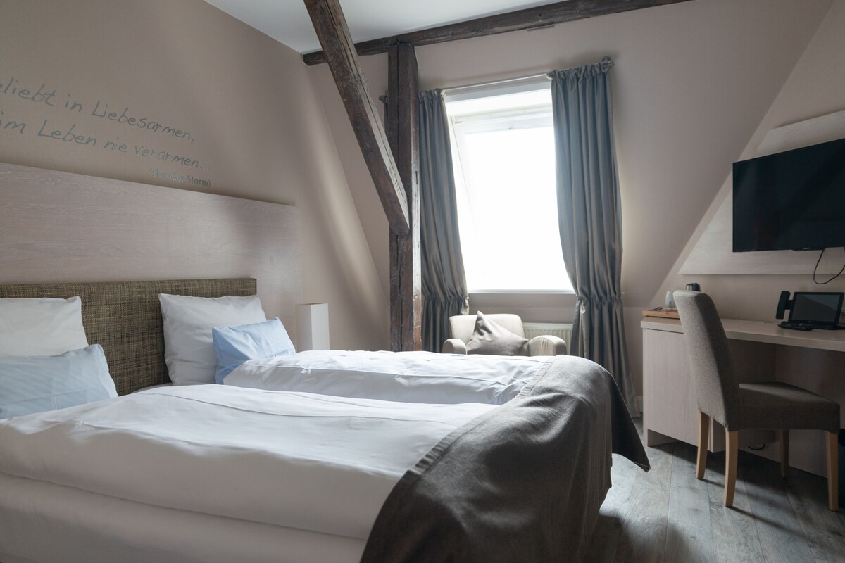 A hotel room with two beds, a desk, a chair, a TV, and a window with curtains.