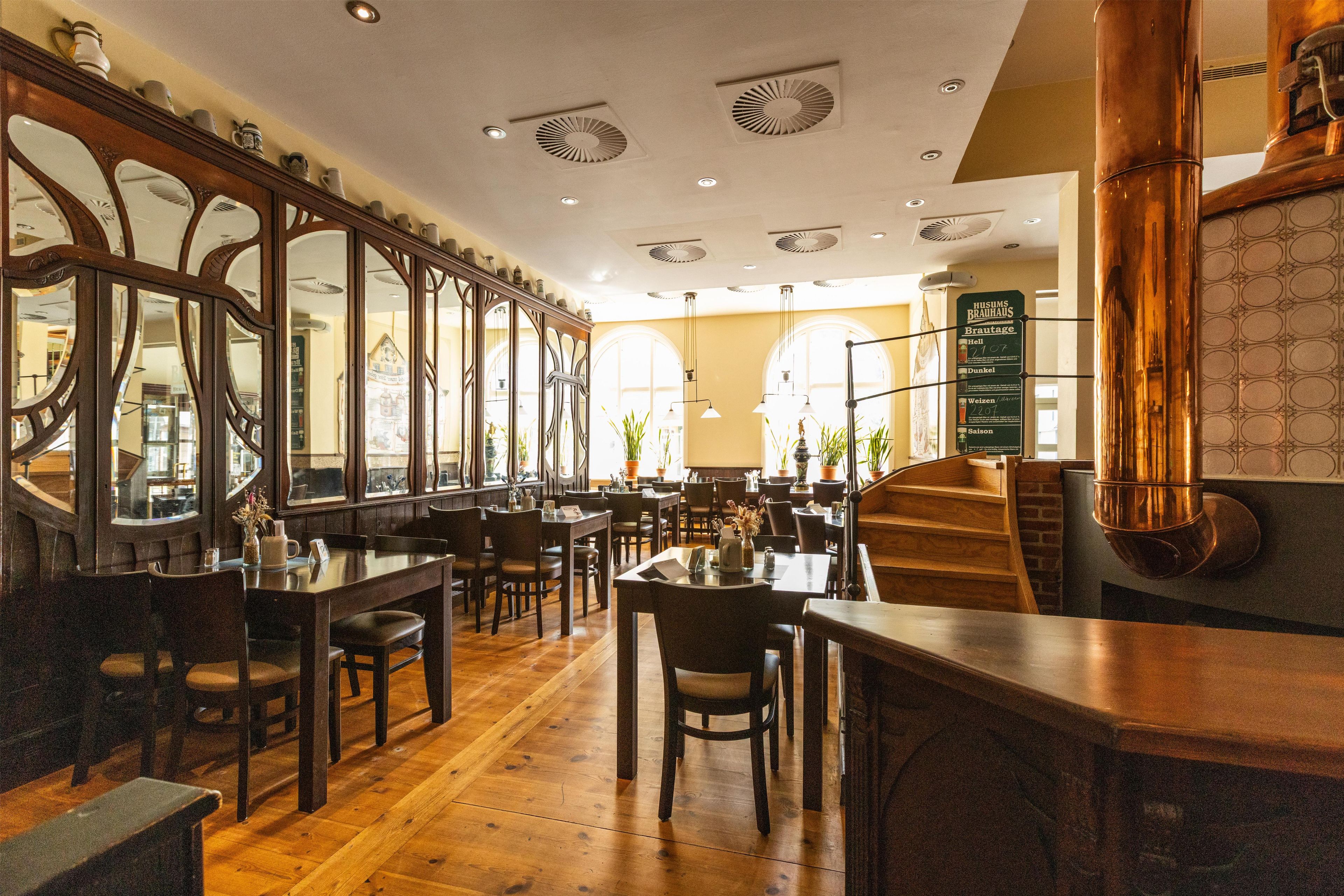Un interior de restaurante con mesas y sillas de madera, una escalera y un panel con la carta.