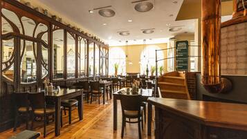 Un interior de restaurante con mesas y sillas de madera, una escalera y un panel con la carta.