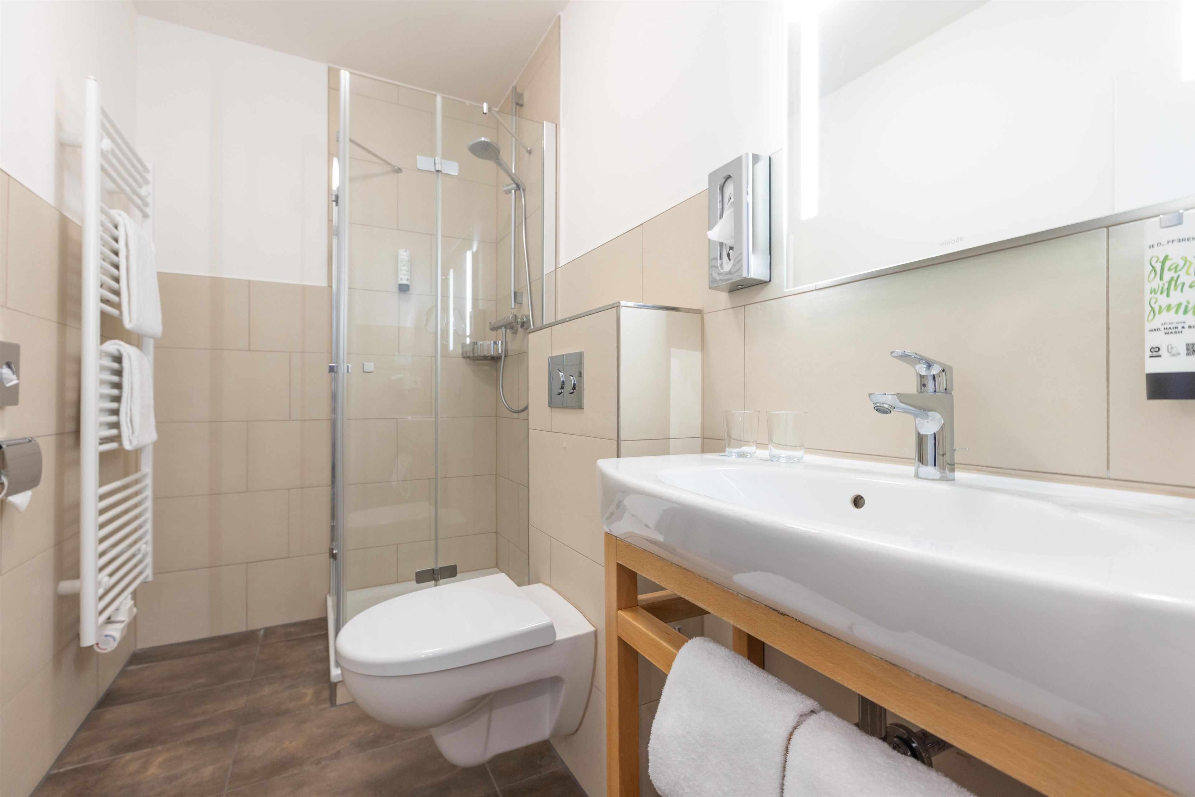 Un baño moderno con cabina de ducha de vidrio, inodoro, lavabo con espejo y un perchero para toallas.