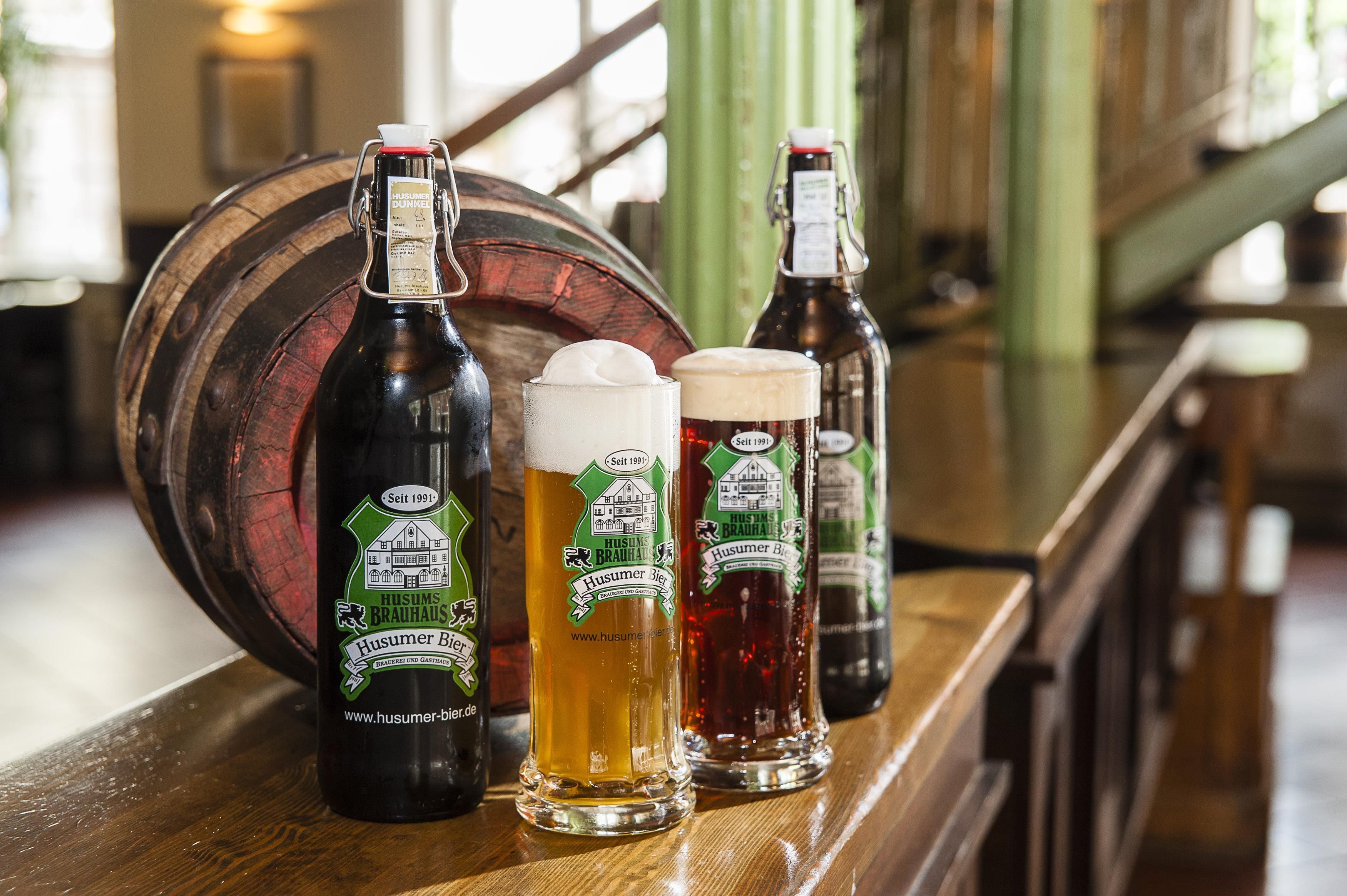Una barra de madera con botellas de Husumer Bier y vasos de cerveza.