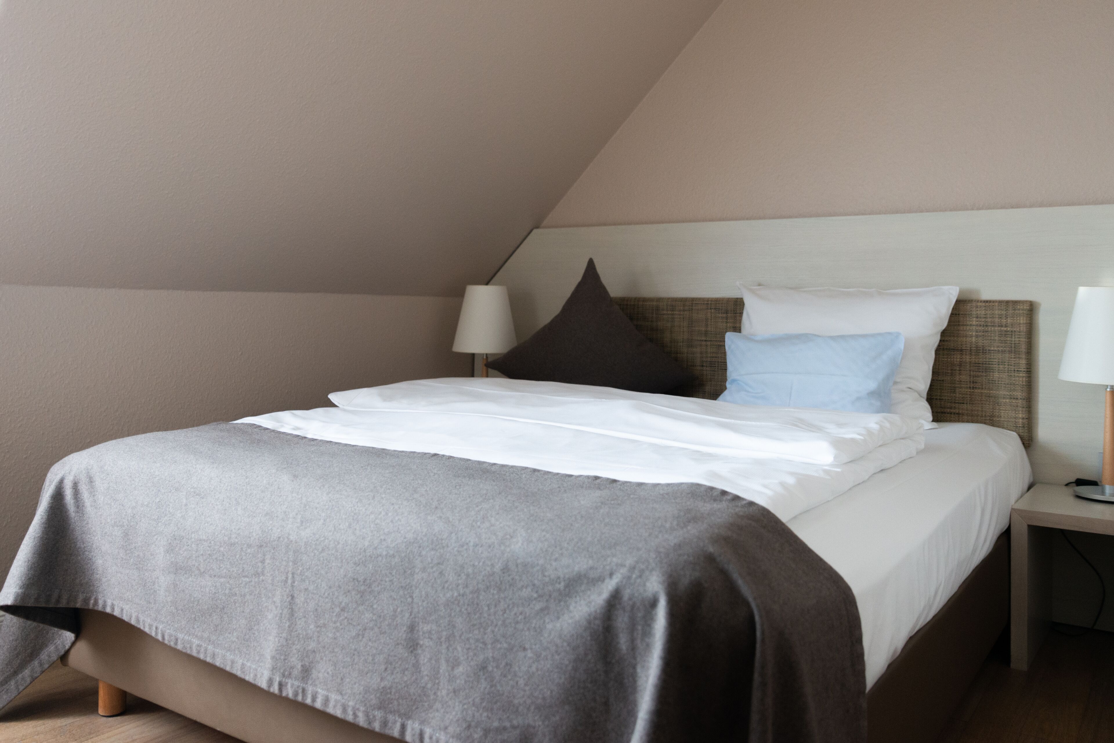 A neatly made bed with a grey bedspread and white linens, a bedside lamp, and a headboard with a brown and beige pattern.