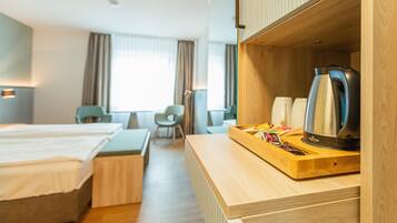 A hotel room with a wooden desk, a kettle, and a tray with snacks. There are two beds and a chair in the room.