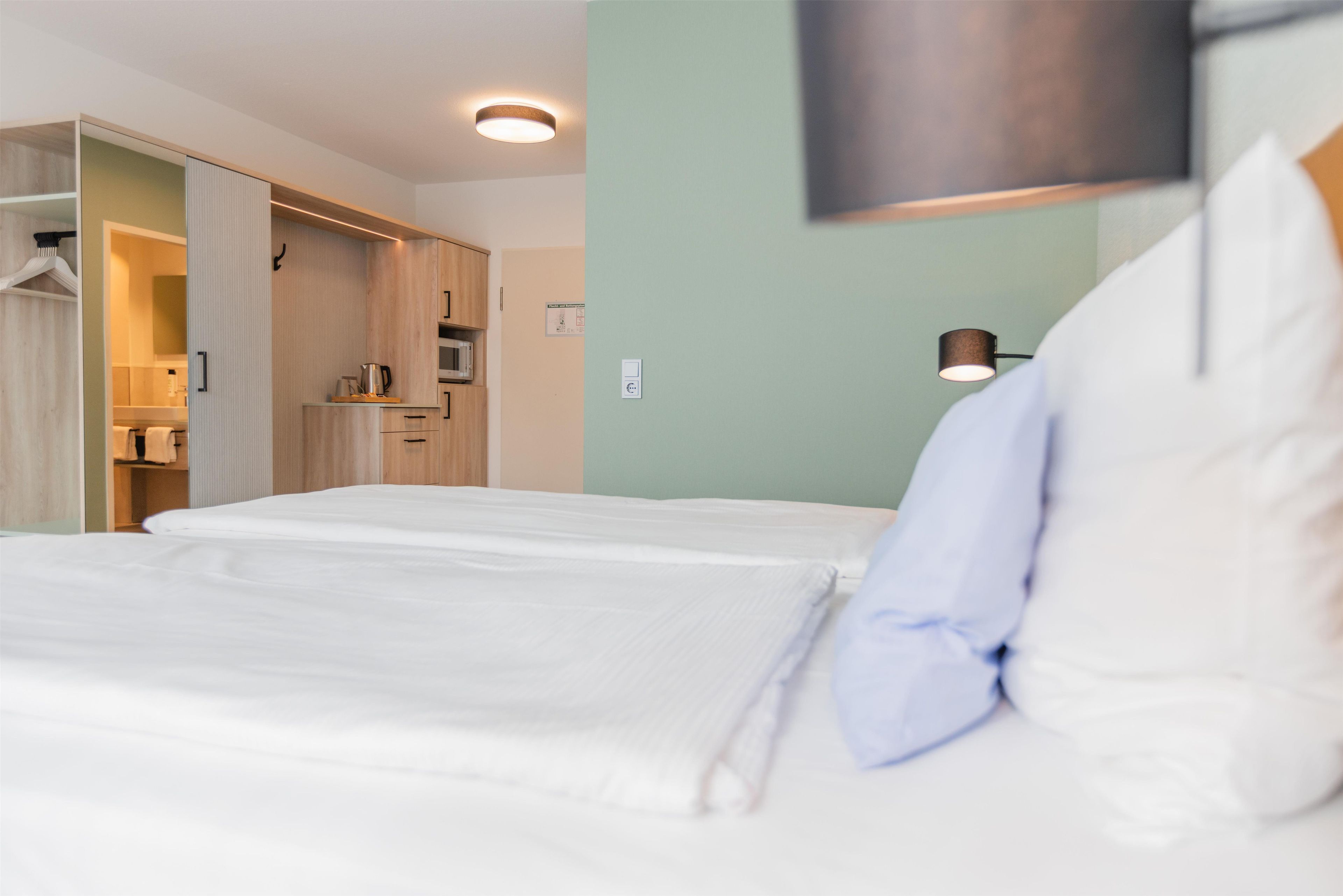 Habitación de hotel con cama, armario, microondas y lámpara.