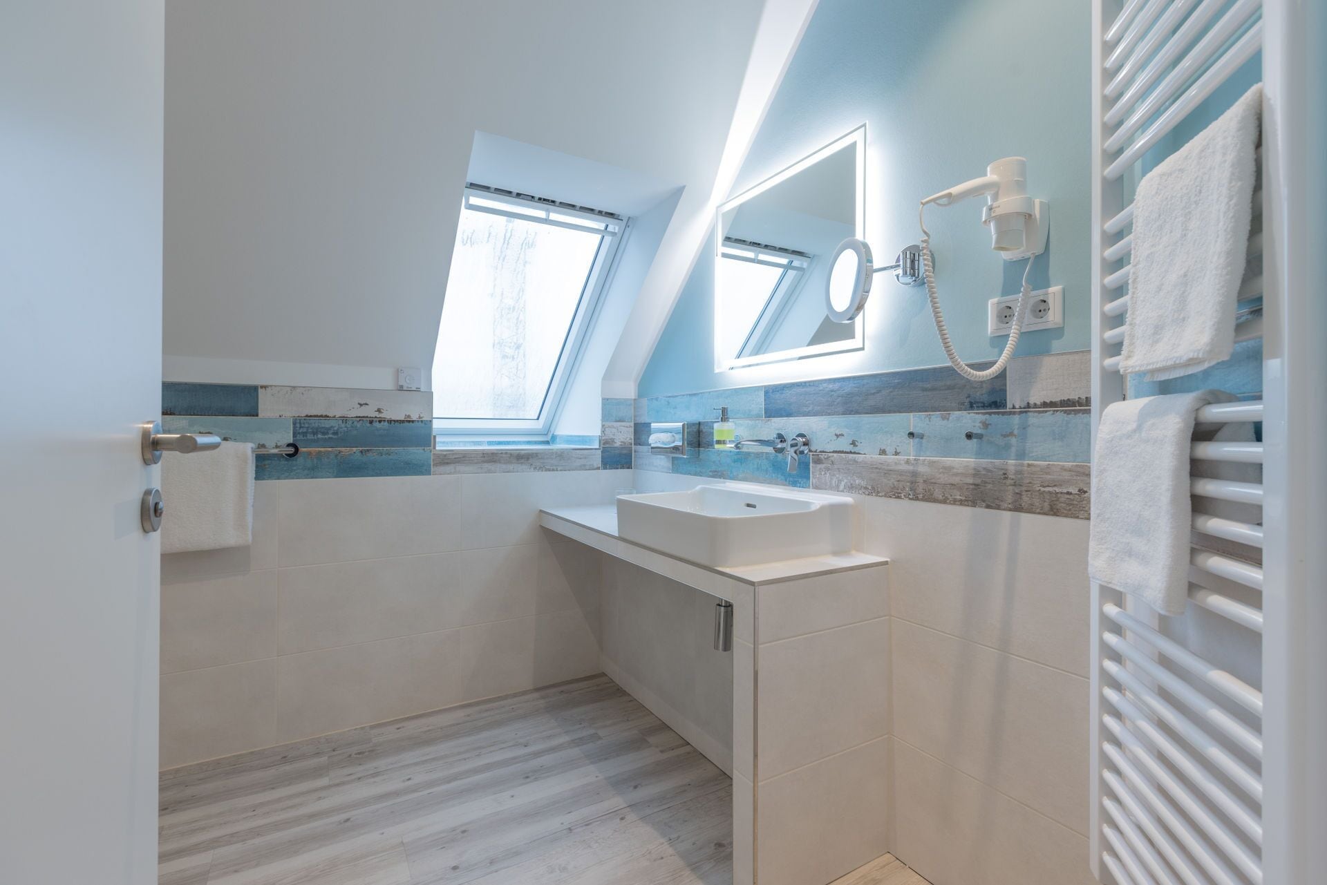 Un baño moderno con tragaluz, un espejo grande, un lavabo y un perchero para toallas.