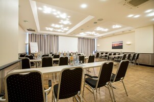 Un salón de conferencias con varias mesas y sillas, una pizarra y un cuadro en la pared.