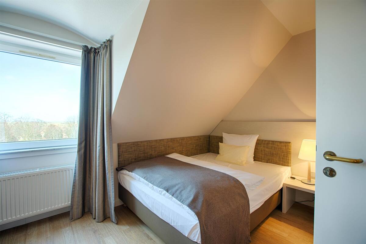 A bedroom with a bed, a nightstand, a lamp, and a window with curtains.