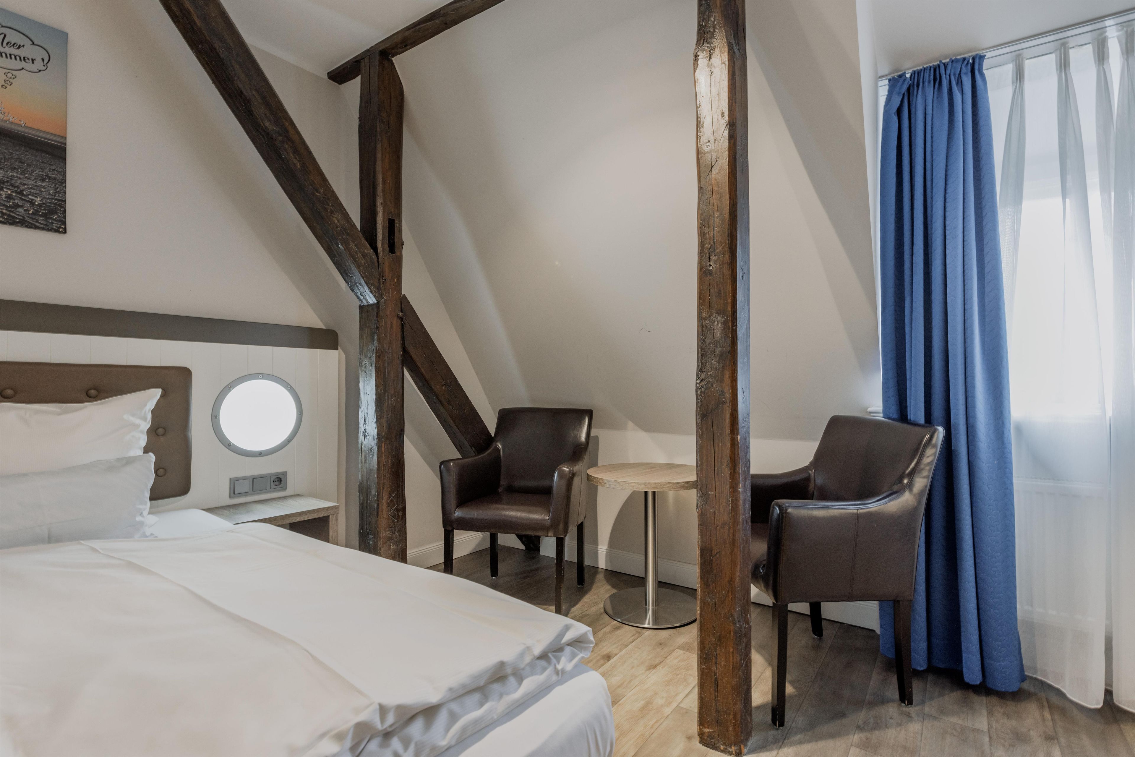 A hotel room with a bed, two chairs, a small table, and a window with curtains.