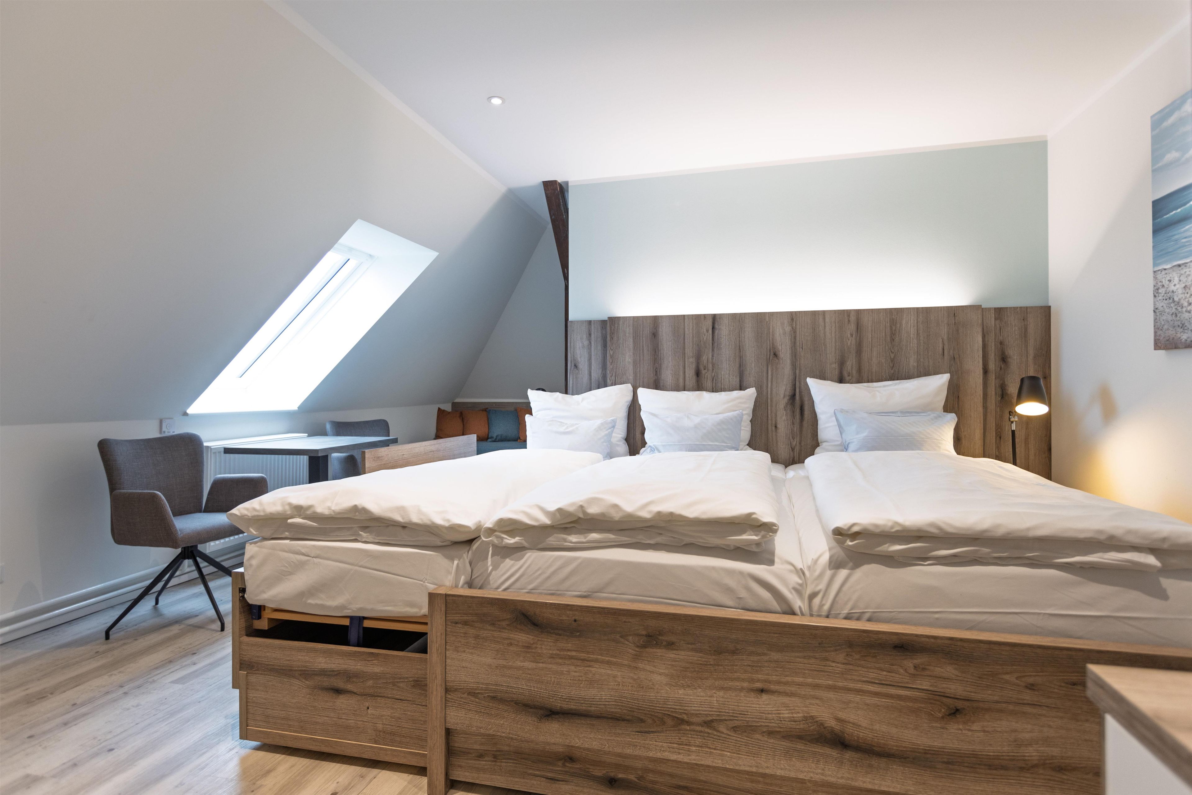 A modern bedroom with a sloped ceiling, a wooden bed frame, and a desk with a chair.
