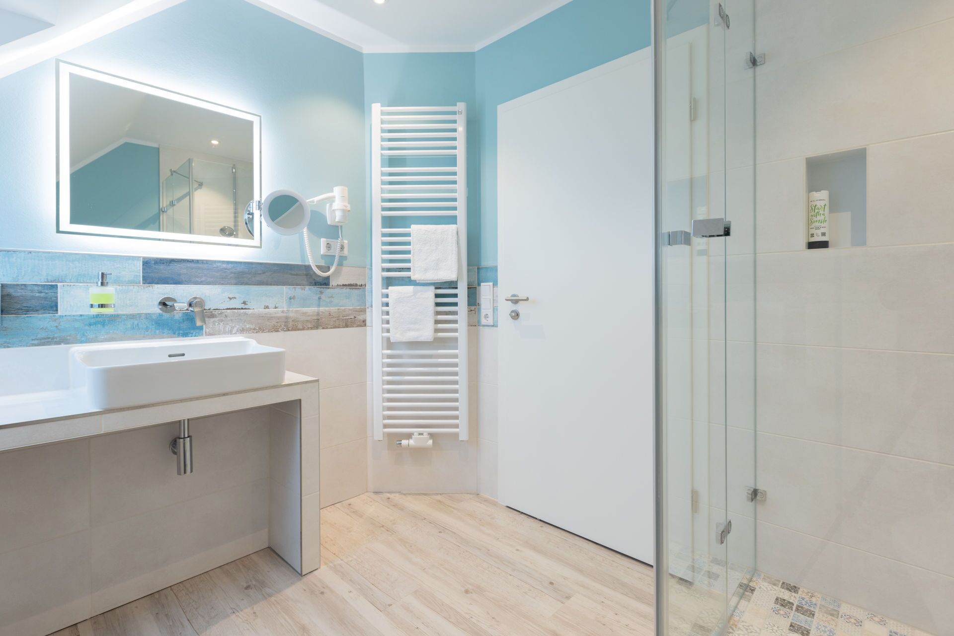 Une salle de bain moderne avec un grand miroir, un lavabo, un porte-serviettes et une cabine de douche en verre.
