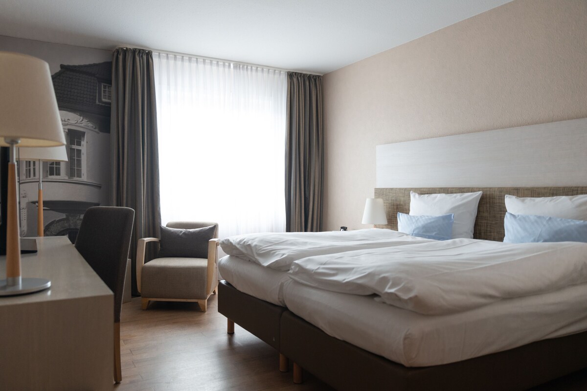A hotel room with a bed, a desk, a chair, and a lamp.