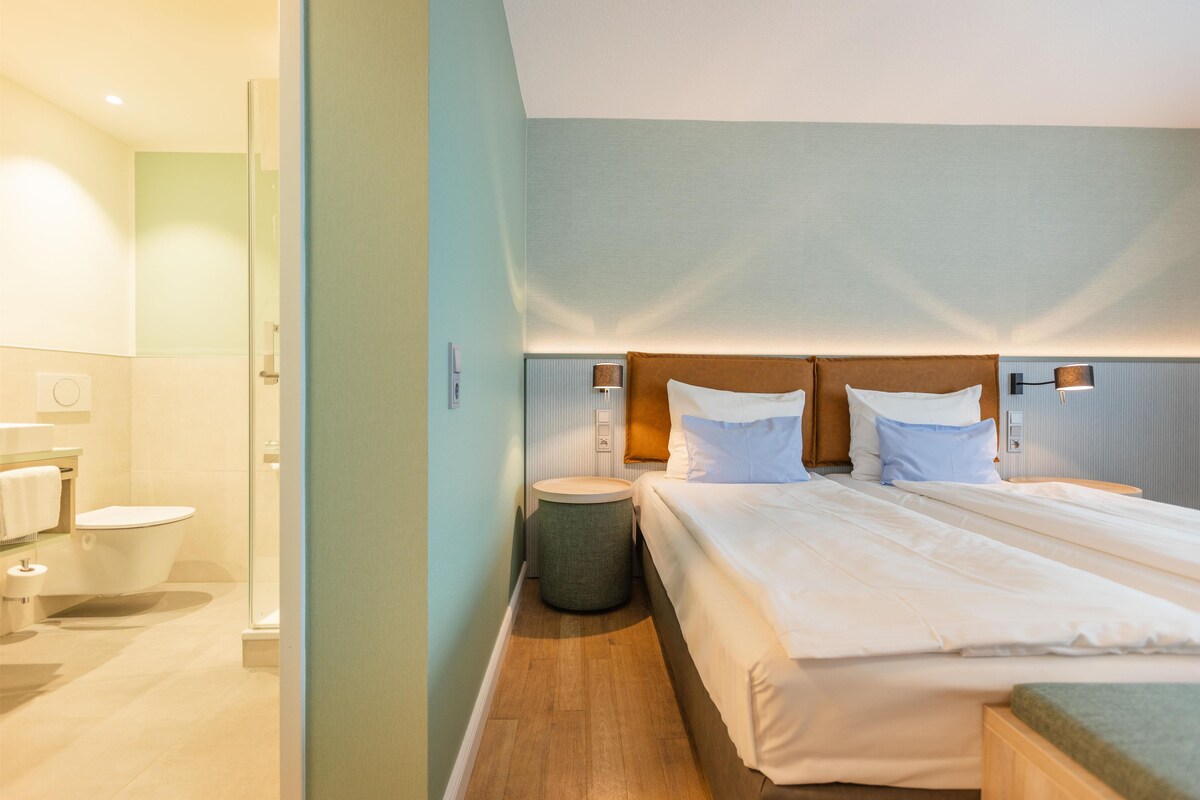A modern hotel room with a large bed, bedside tables, a small round table, and a separate bathroom area.