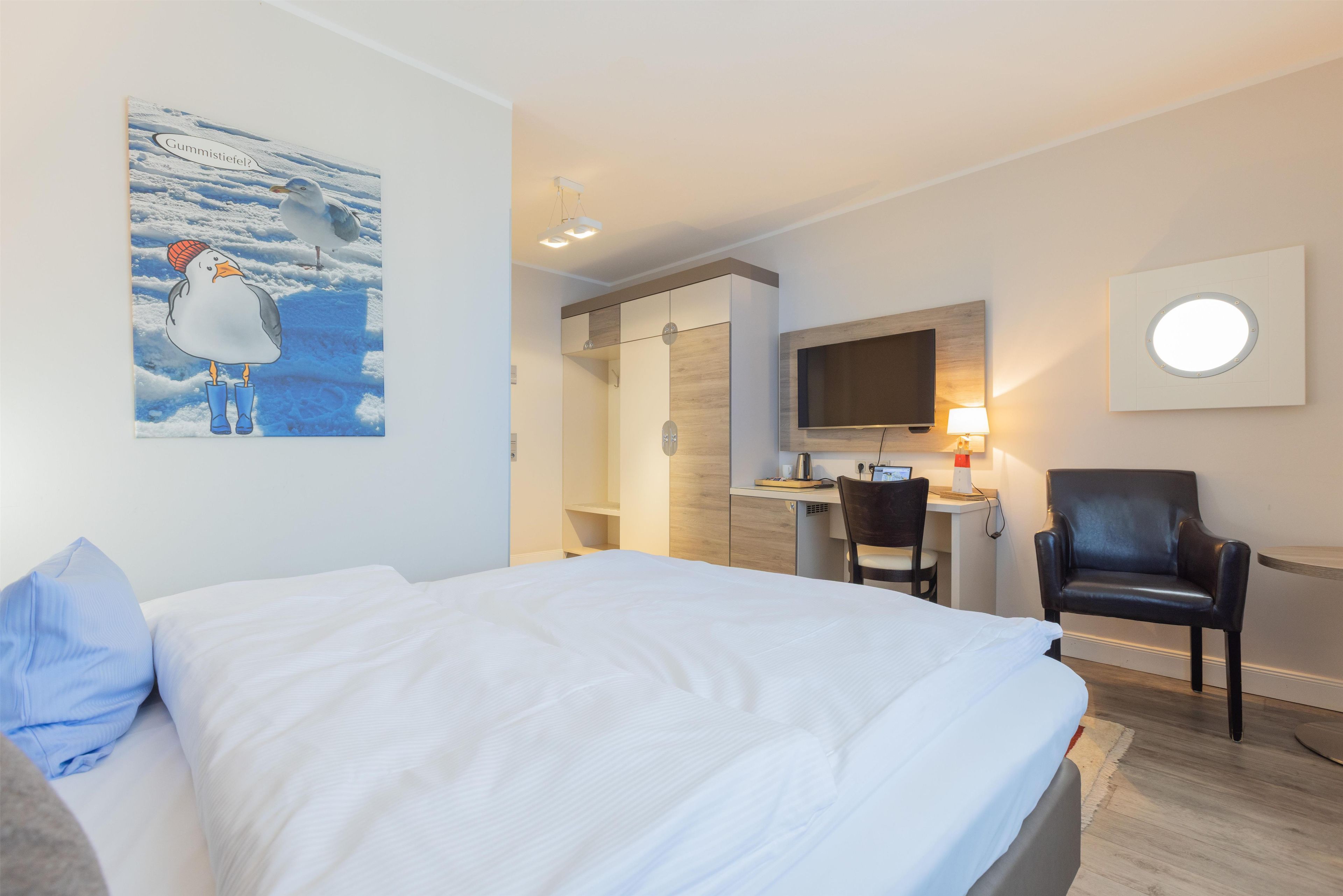 Una habitación de hotel con cama, escritorio con computadora, silla, televisor y un cuadro en la pared.