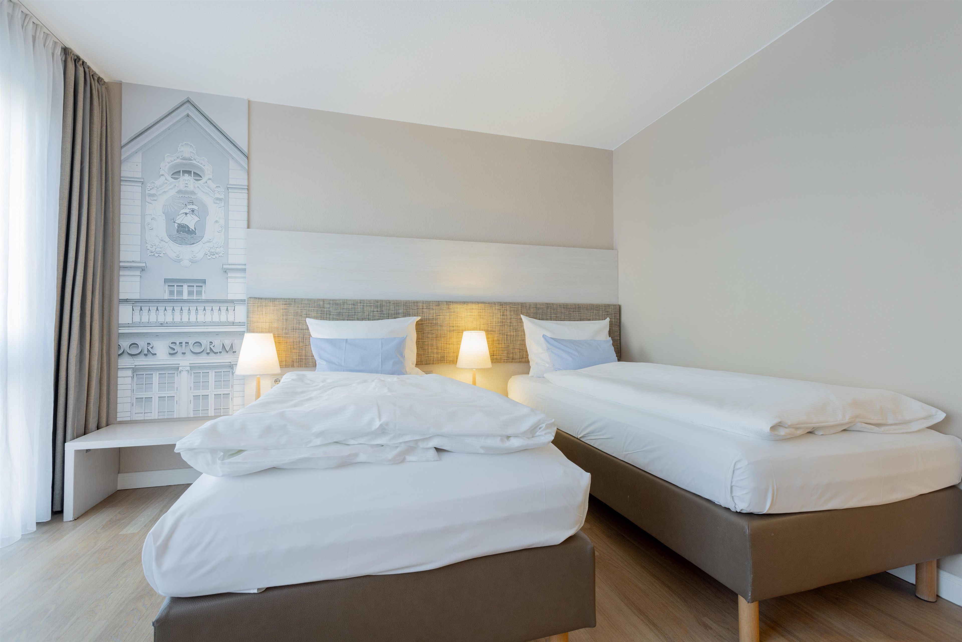 Habitación de hotel con dos camas, un banco y un mural en la pared.