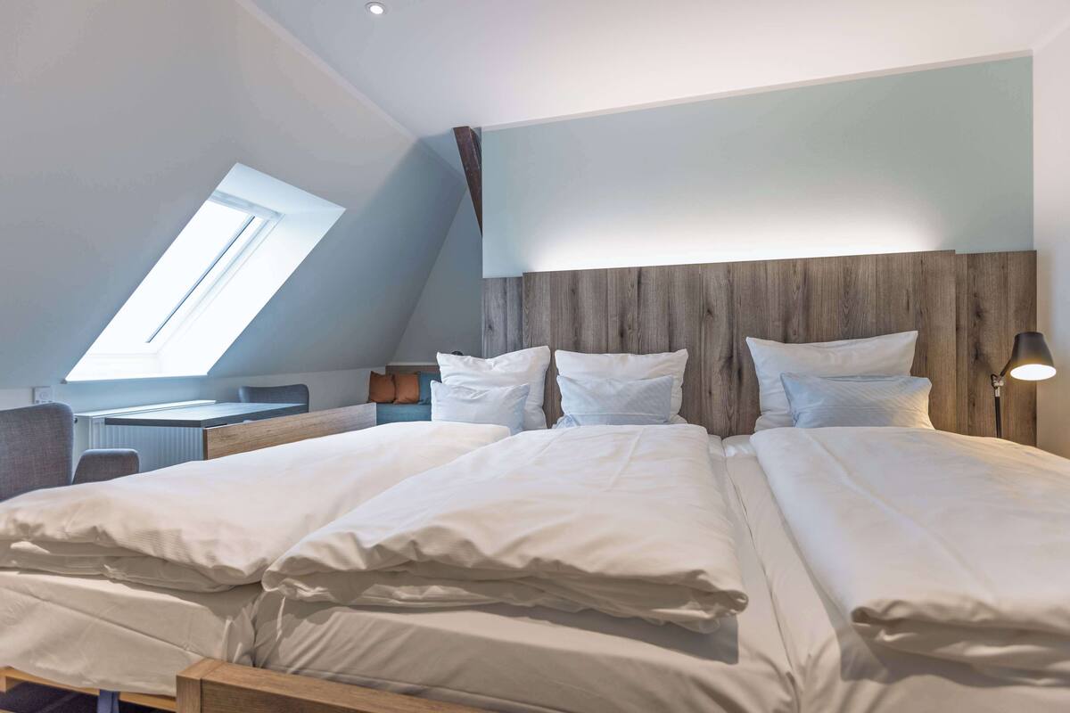 A bedroom with a sloped ceiling, a desk, a chair, and a bed with multiple pillows.