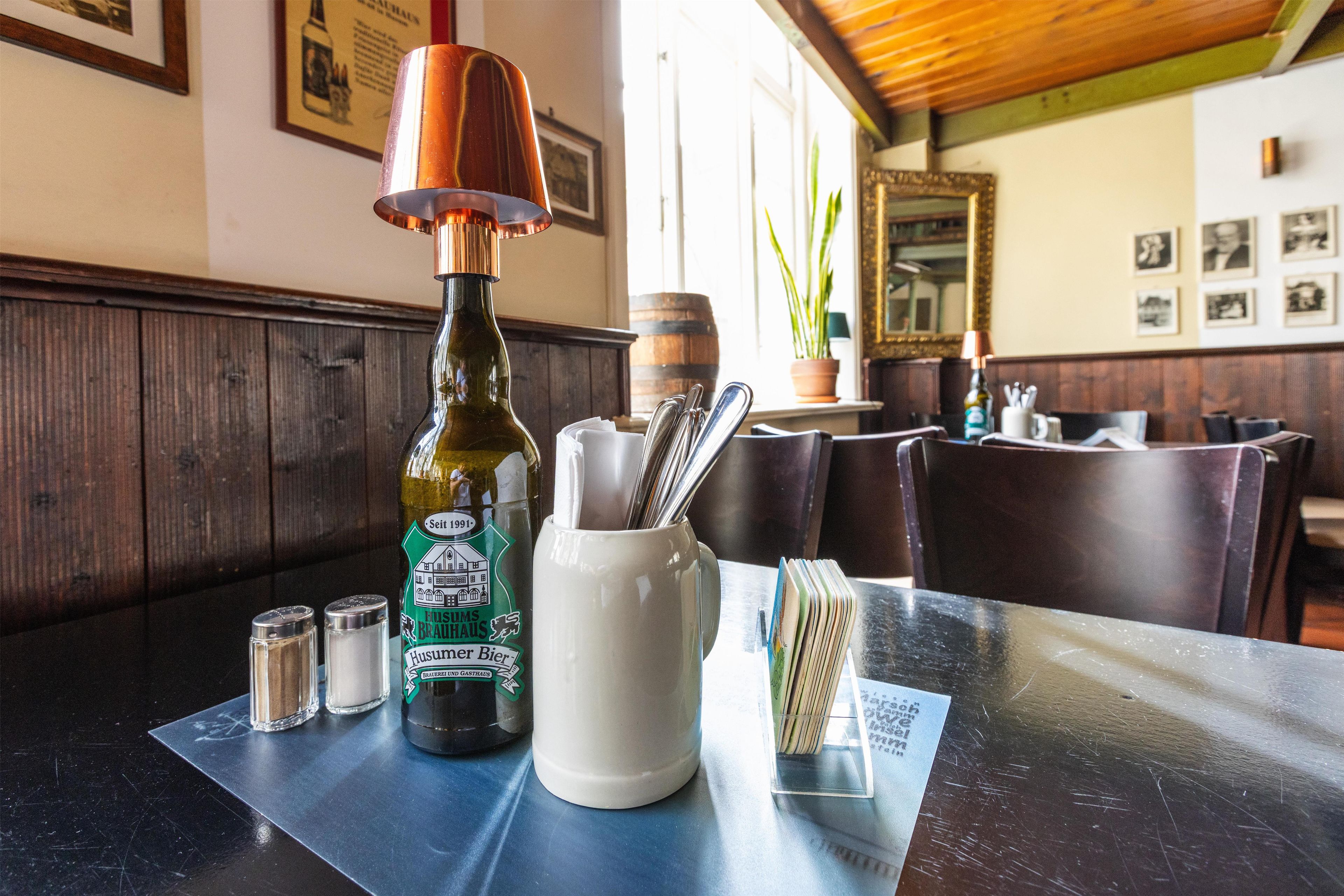 Una mesa con una botella de Husumer Bier, saleros y pimenteros, una taza blanca y un menú.