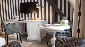 Una habitación con una pared a rayas, un escritorio con una computadora, una silla, una mesa con una revista y un jarrón decorativo.