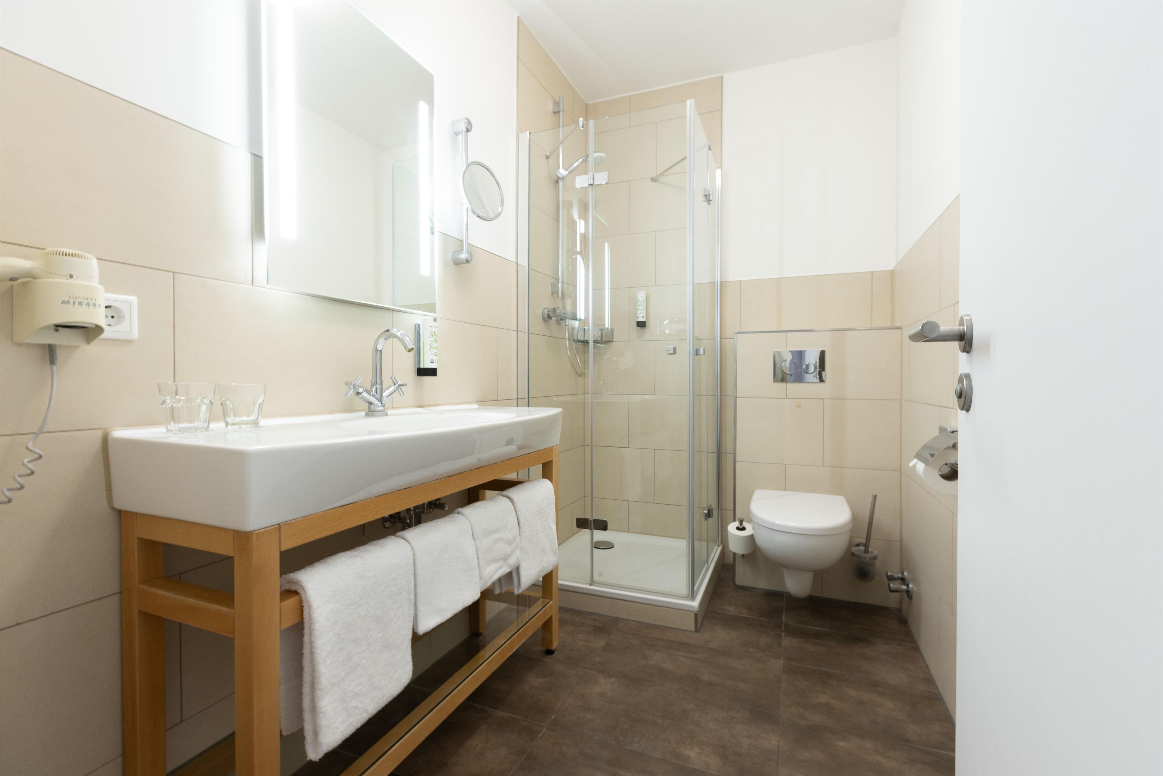 A modern bathroom with a wooden vanity, a glass shower enclosure, and a toilet.