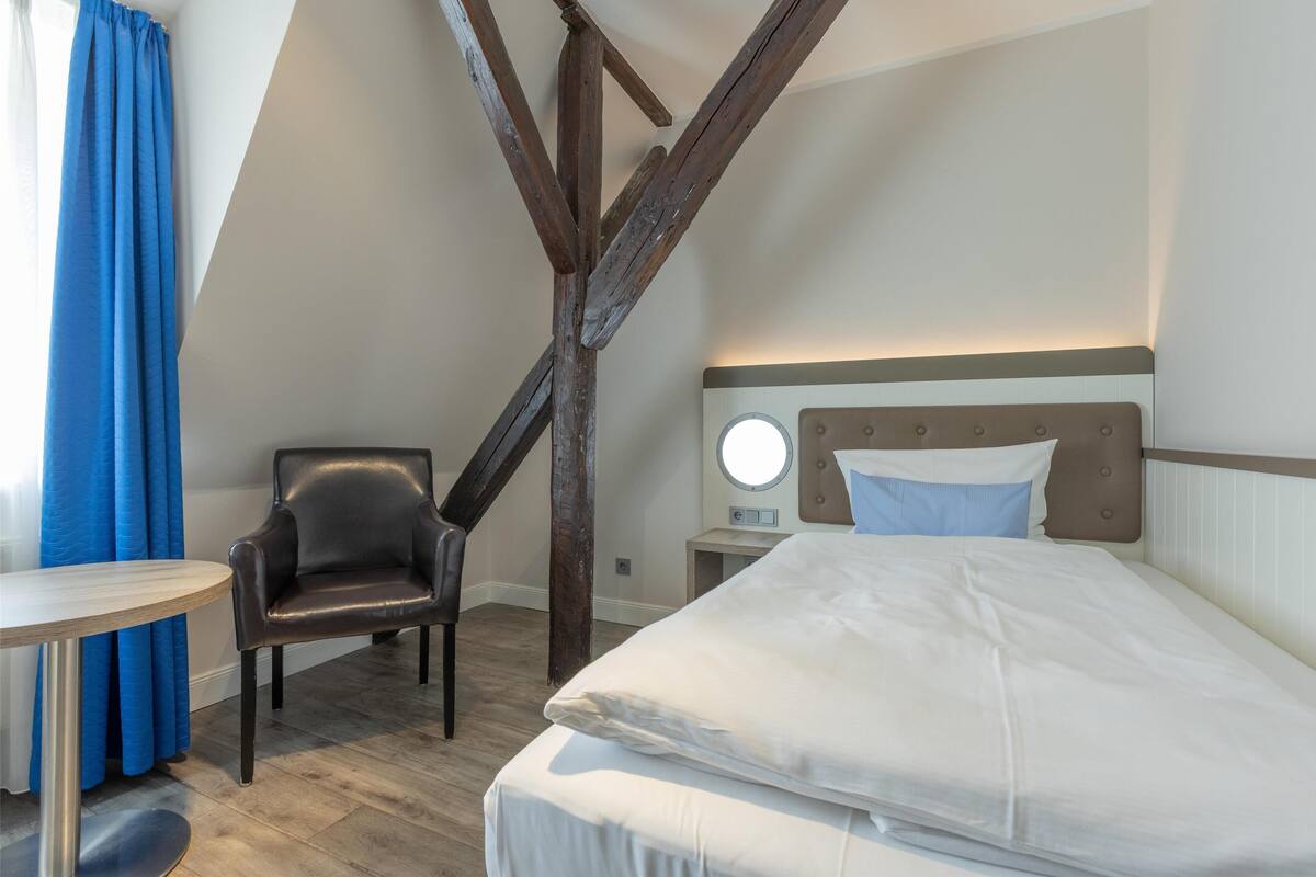 A bedroom with a bed, a chair, a table, and a nightstand.