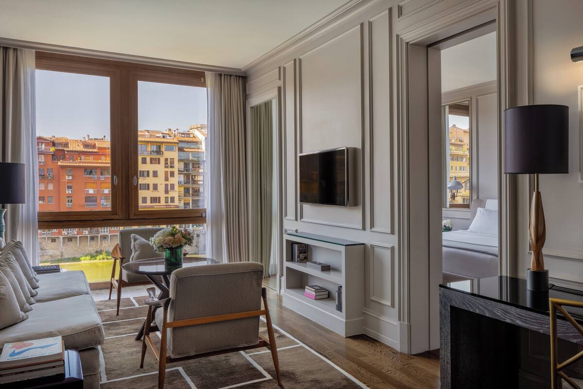 Una habitación de hotel moderna con sofá, sillón, televisor y balcón con vistas a la ciudad.