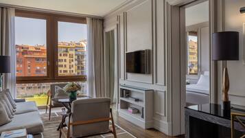 A modern hotel room with a sofa, armchair, TV, and a balcony with city views.