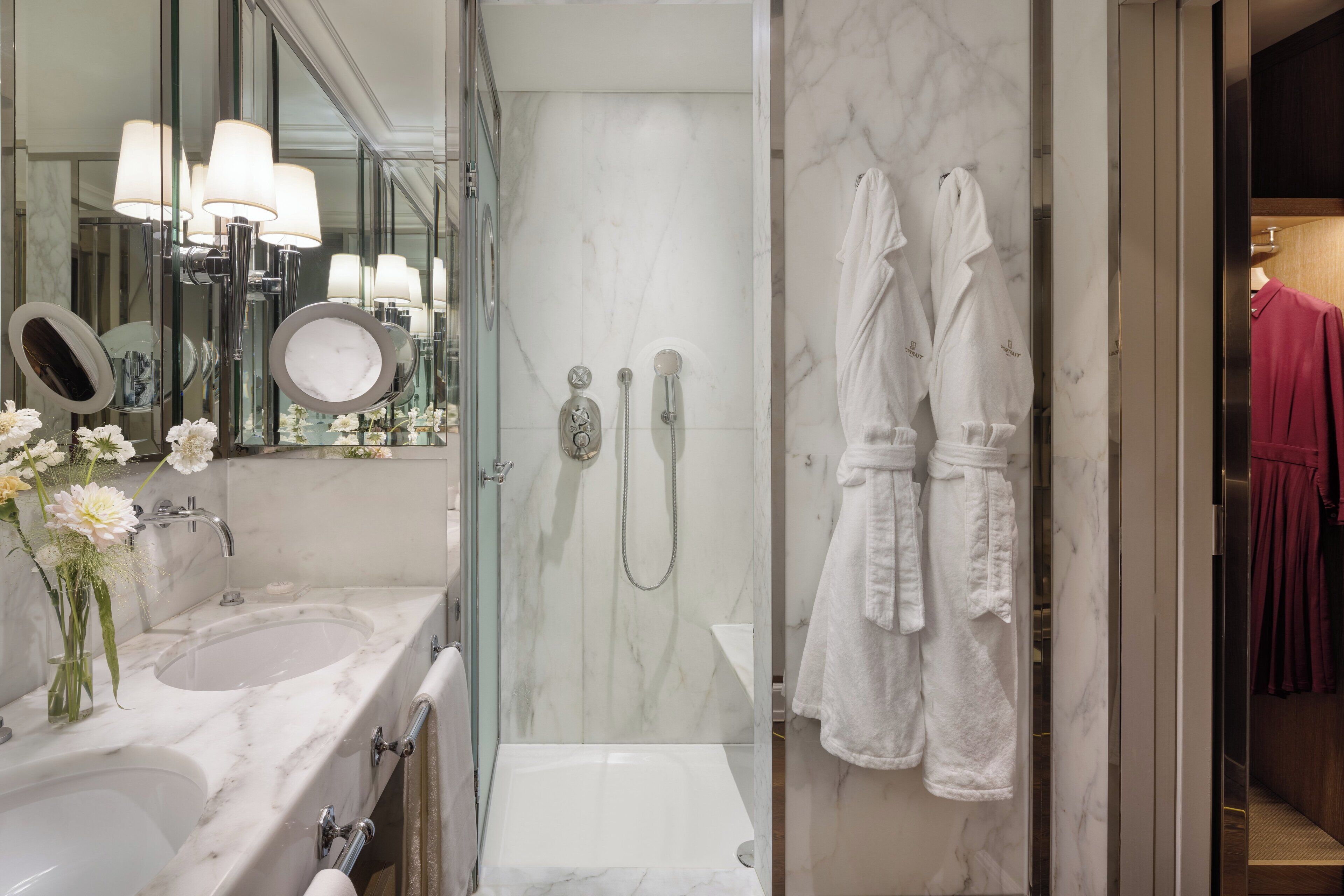 A modern bathroom with a glass-enclosed shower, a large mirror, and a vanity with a sink and a vase of flowers.
