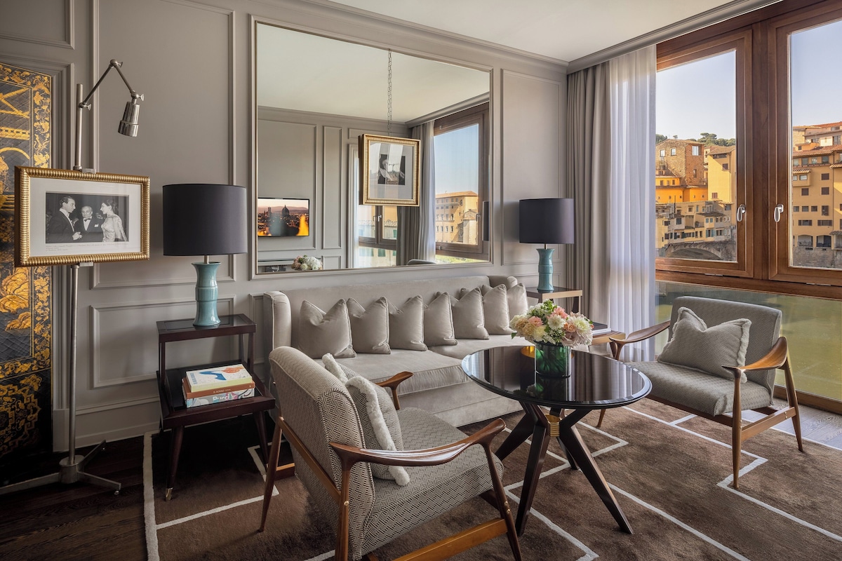 A modern living room with a sofa, two armchairs, a coffee table, and a large window offering a city view.