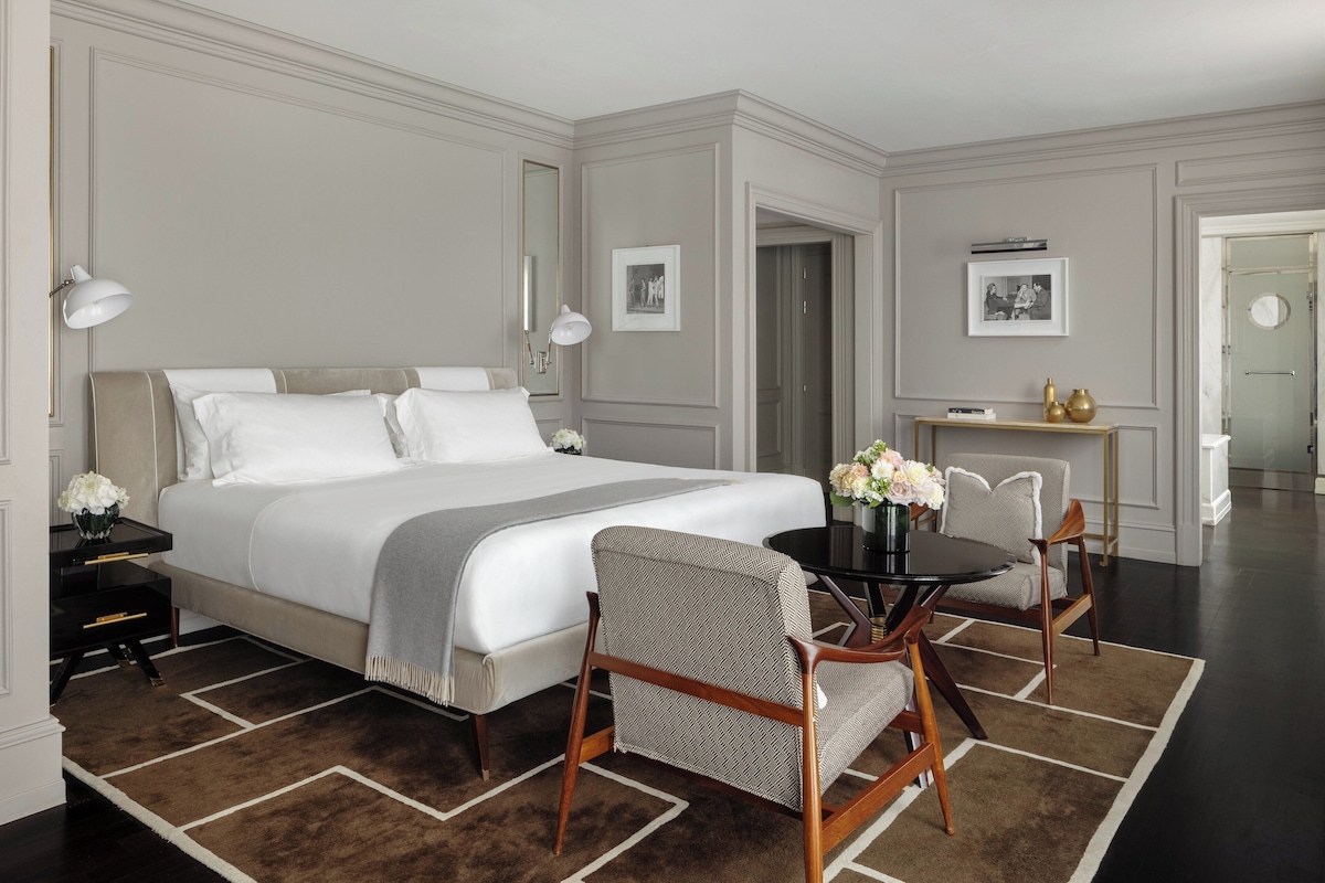 A hotel room with a large bed, a dining table with chairs, a small side table, and a mirror.