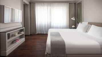 Een hotelkamer met een groot bed, een aan de muur bevestigde televisie, een boekenkast en een raam met gordijnen.